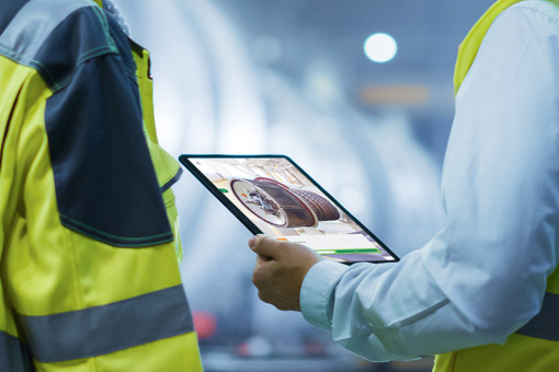 Two workers in high-visibility vests reviewing equipment information on a tablet